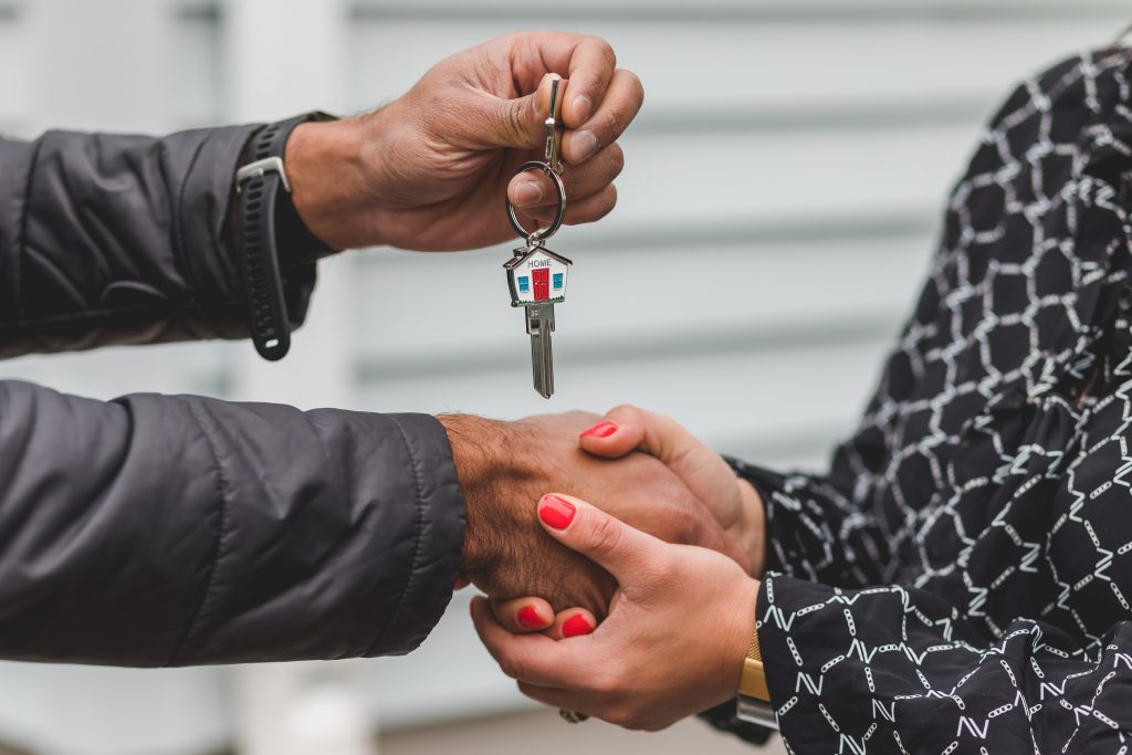 One person handing a house key to another person, representing the exchange of property that a Grant Deed accomplishes.