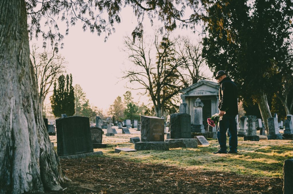 Man with flowers in a cemetery, symbolizing a certified copy of a death certificate from Alameda County.